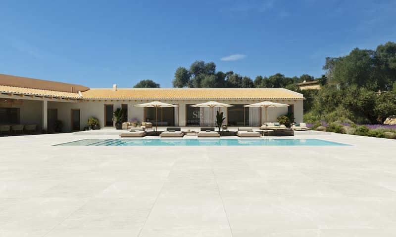 Gran piscina y amplia terraza de tonos claros frente a una villa mediterránea bajo un cielo azul despejado.