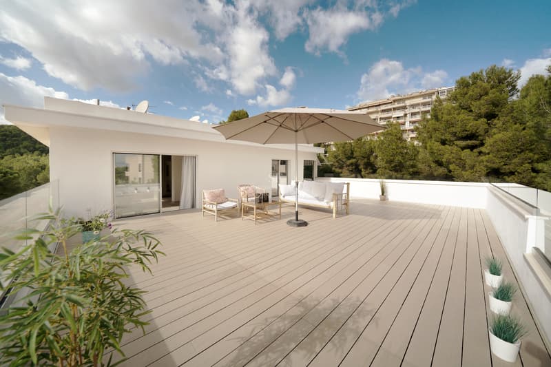 Terraza espaciosa con tarima de madera, muebles de exterior blancos y barandillas de cristal bajo un cielo despejado.