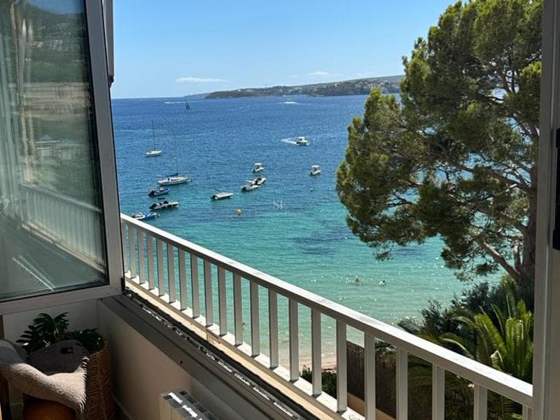 Panoramautsikt över bukten med båtplatser Utsikt från en balkong över en turkos medelhavsbukt med vita yachter, en tall och ett vitt räcke.