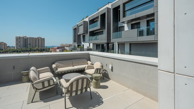 Amplia terraza moderna con mobiliario de exterior en color beige, suelo de gres gris y vistas a edificio contemporáneo.