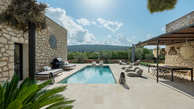 Piscine rectangulaire turquoise entourée d'une terrasse en pierre, coin repas extérieur et murs en pierre naturelle.