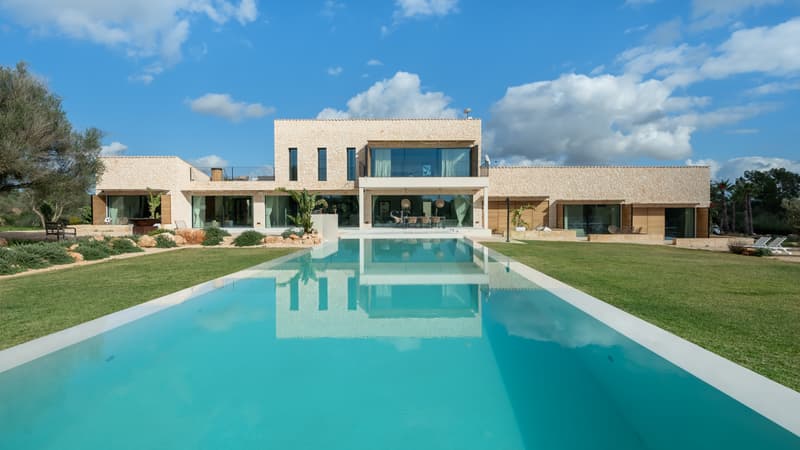 Moderne zweistöckige Villa mit einem großen rechteckigen Pool und Natursteinfassade unter blauem Himmel.
