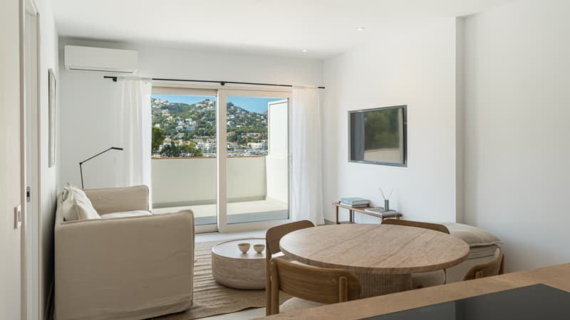 Modernes Wohnzimmer mit hellen Holzmöbeln und großen Glasschiebetüren, die auf eine Terrasse mit Blick auf die Bucht führen.