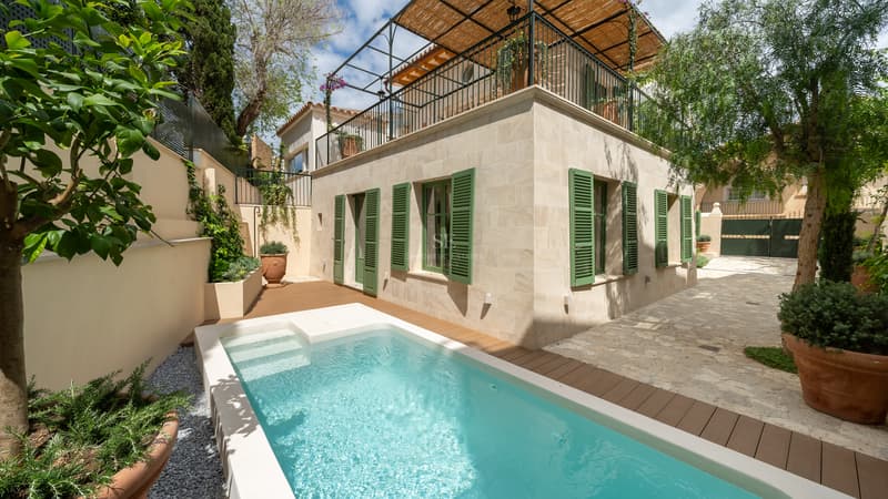 Villa de piedra con piscina turquesa, terraza de madera y persianas tradicionales verdes en Mallorca.
