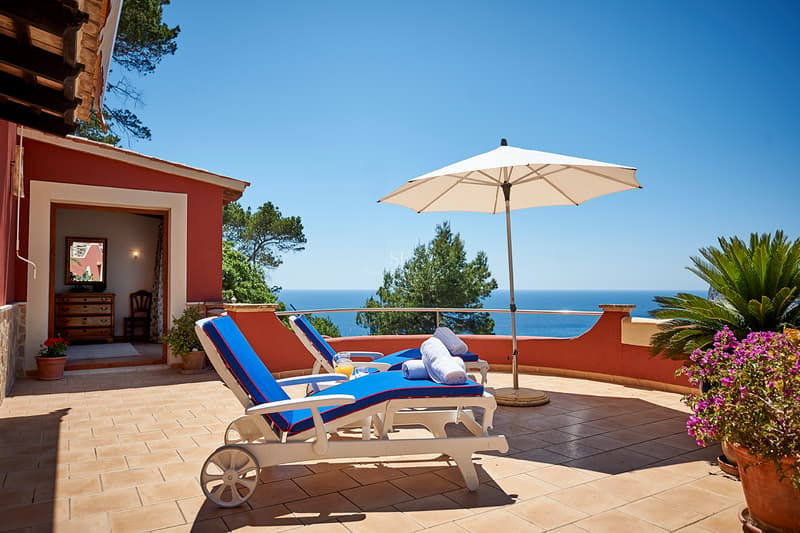 Sunny Mediterranean Terrace with Panoramic Sea View Two blue sun loungers on a terracotta terrace overlooking a bright blue ocean under a clear sky.
