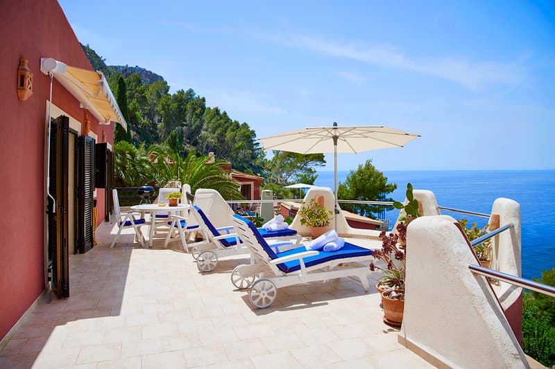 Luxury Mediterranean Terrace with Sea Views Sunny terrace with blue loungers, white umbrella, and panoramic views of the Mediterranean Sea and cliffs.