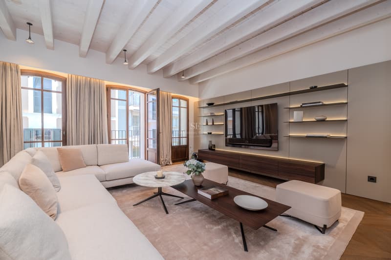 Salón de lujo con techos de vigas blancas, sofá en L, mueble de televisión integrado y ventanales franceses.
