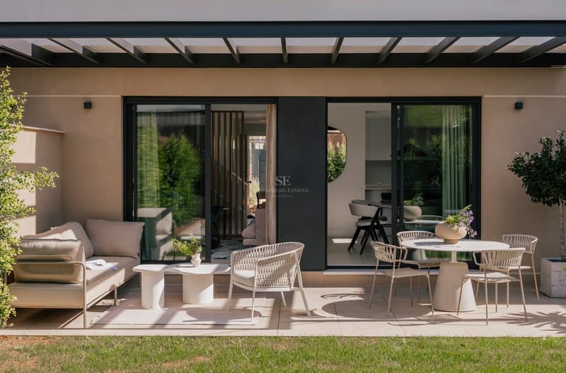 A contemporary terrace with beige outdoor furniture, a black pergola, and sliding glass doors leading into the home.