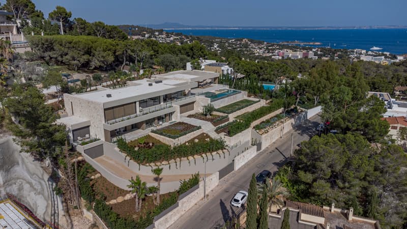 Aerial view of a contemporary multi-level villa with natural stone walls, infinity pool, and Mediterranean sea views.