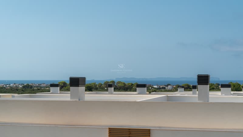 Vistas Panorámicas al Mar y la Isla desde el Solárium Vista desde una azotea blanca moderna hacia el mar Mediterráneo azul y una isla lejana sobre un bosque de pinos.