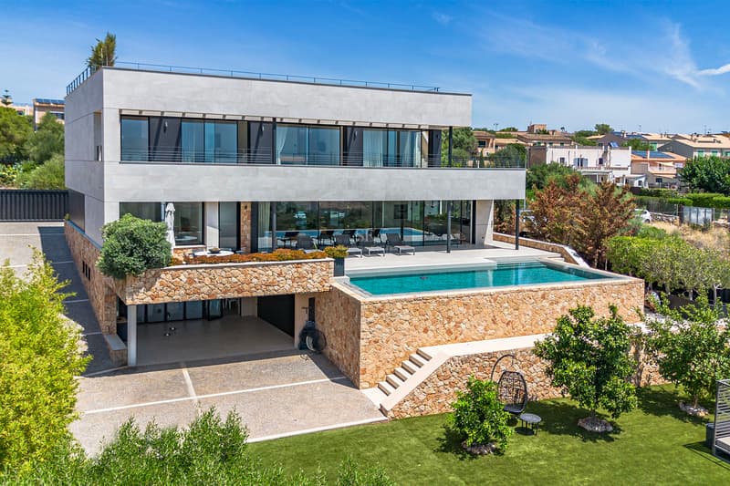 Modern trevåningsvilla med turkos infinitypool, naturstensväggar och stora glaspartier.
