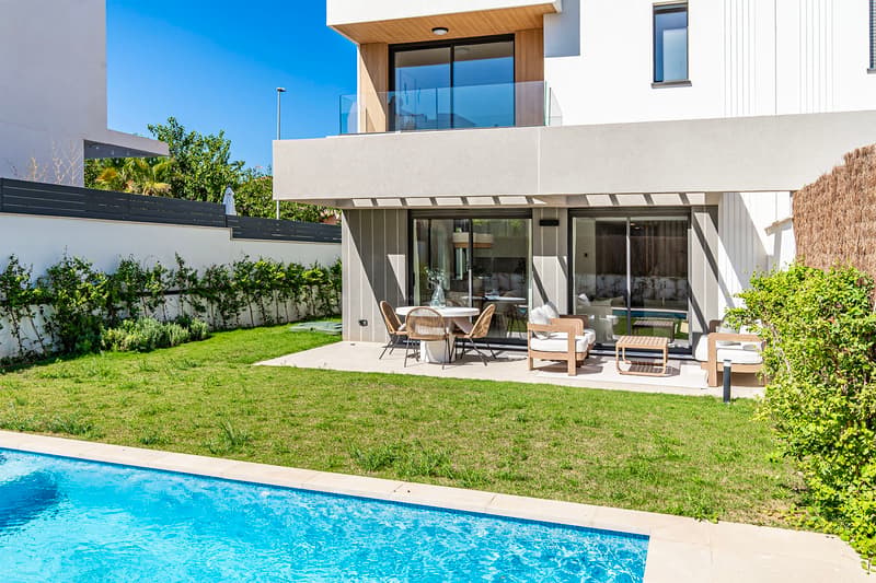 Samtida villa med turkos pool, välskött gräsmatta och skuggig terrass med designmöbler.