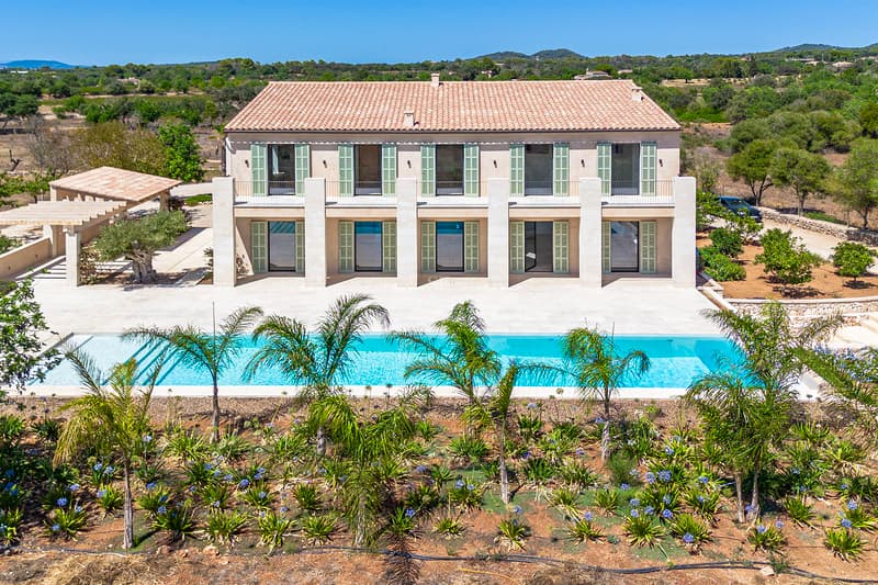 Fachada de villa de lujo con persianas verdes, piscina rectangular y jardín mediterráneo bajo un cielo despejado.
