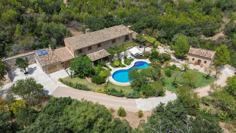 Aerial View of Secluded Mediterranean Stone Villa Aerial shot of a stone villa with a blue pool, guest house, and gardens surrounded by green forest.