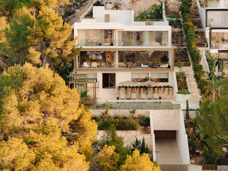 Dreistöckige moderne Villa am Hang mit großen Glasfronten, Infinity-Pool und Natursteinmauern.