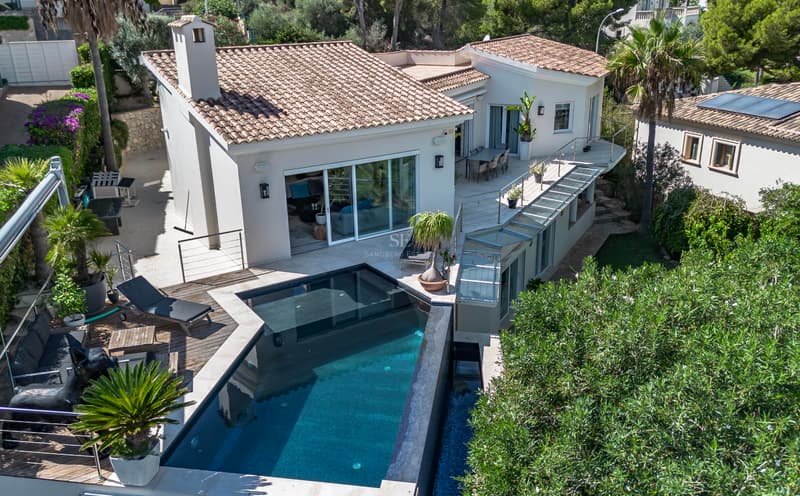Vista aérea de una villa blanca con tejado de teja, piscina infinita de tonos oscuros y amplias terrazas de madera.