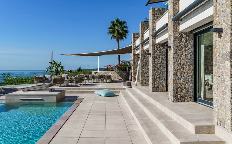 Luxuriöse Steinterrasse mit Infinity-Pool, schattigem Loungebereich und weitem Blick über das Meer.