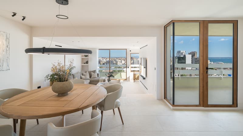 Salón y comedor moderno y luminoso con muebles de madera y grandes ventanales con vistas al mar y la ciudad.