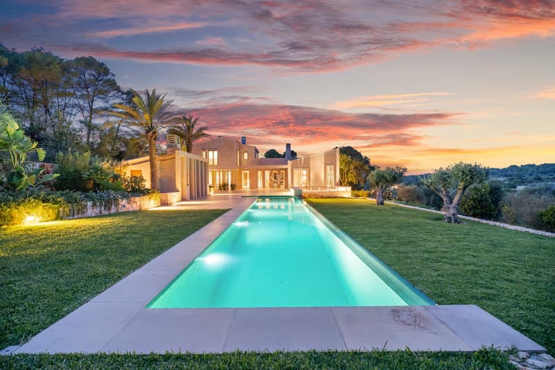 Luxury Villa with Lap Pool at Sunset A long, illuminated rectangular pool leading to a modern stone villa under a vibrant pink and orange sunset sky.