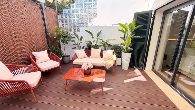 Terrasse mit Holzdielen, terracottafarbenen Gartenmöbeln und dekorativen Pflanzen bei Tageslicht.