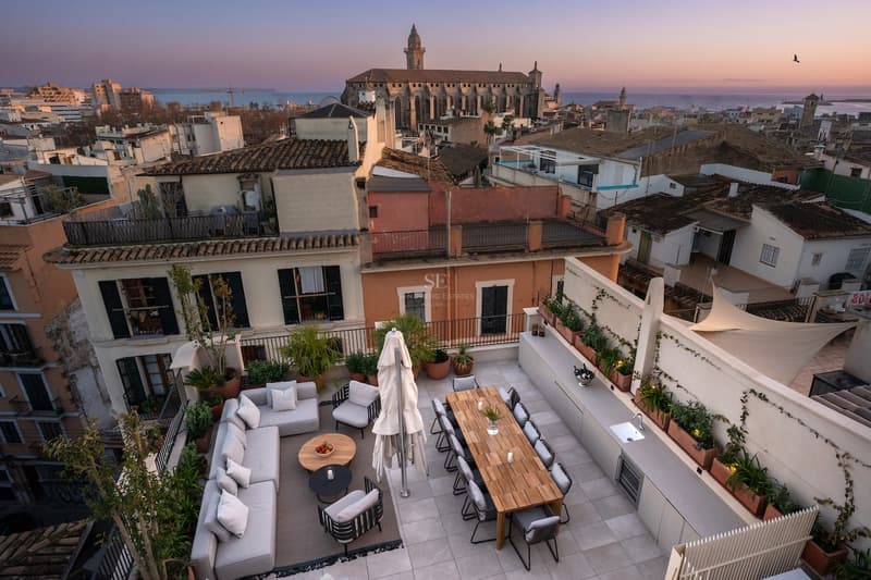 Terraza de Lujo en la Azotea con Vistas a la Catedral Elegante terraza en la azotea con sofás, mesa de comedor y cocina exterior frente a una catedral histórica al atardecer.