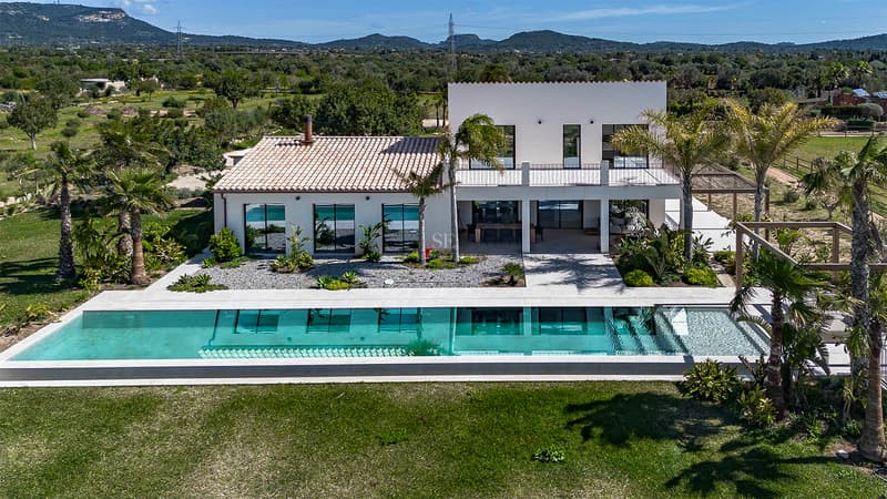 Aerial view of a modern white villa with a turquoise swimming pool and mountains in the background.