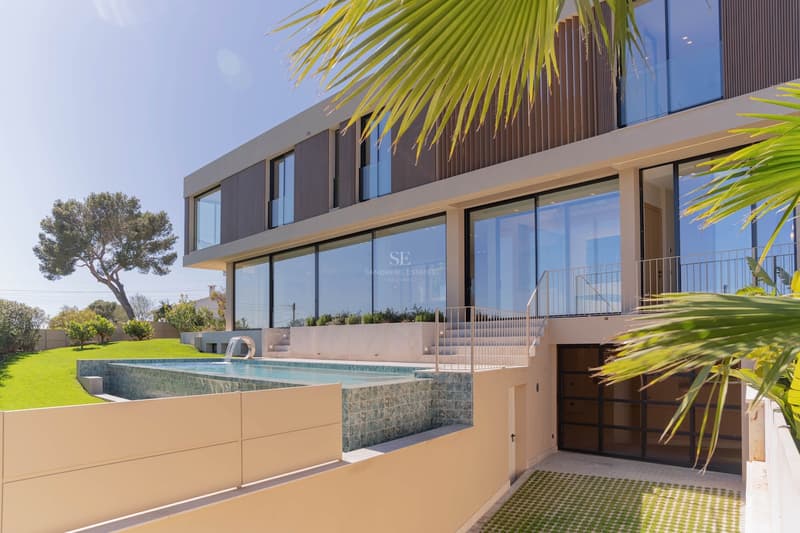 Exteriör av en modern villa med infinitypool, stora glaspartier och grönskande trädgård.