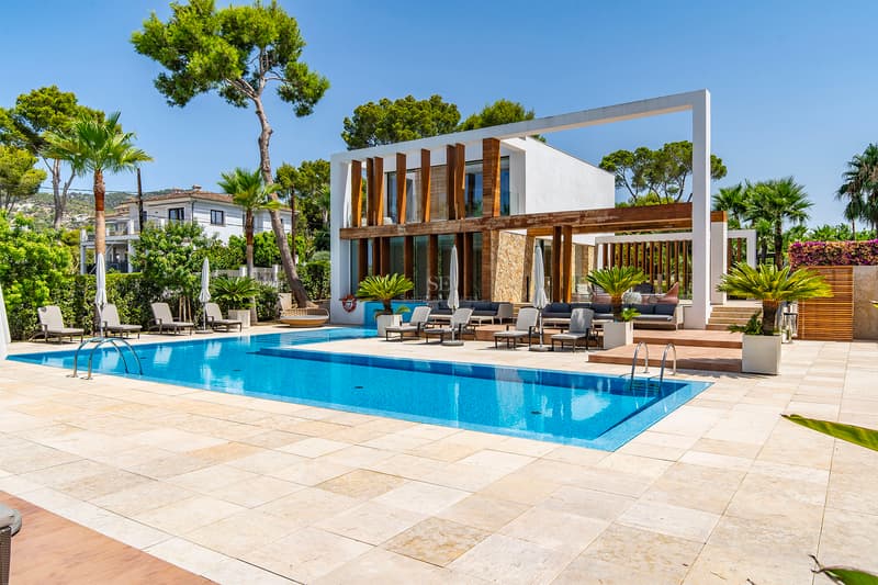 Villa de Luxe Moderne avec Grande Piscine et Solarium Grande piscine bleue entourée d'une terrasse en pierre claire et d'une villa blanche moderne avec accents en bois.