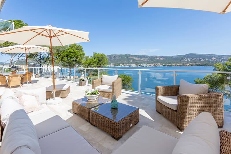 Terrasse de Luxe avec Vue Panoramique sur la Mer Terrasse ensoleillée avec mobilier en osier, parasols blancs et balustrade en verre surplombant la mer.