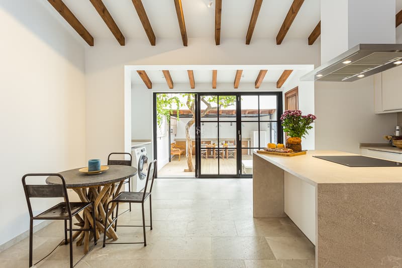 Cuisine Rustique Moderne avec Accès Cour Cuisine lumineuse avec poutres en bois, îlot en pierre et portes vitrées s'ouvrant sur un patio avec un arbre.