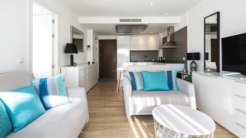 Salon Moderne à Plan Ouvert avec Cuisine Salon lumineux avec canapés blancs, coussins turquoise, parquet en bois et cuisine moderne en arrière-plan.