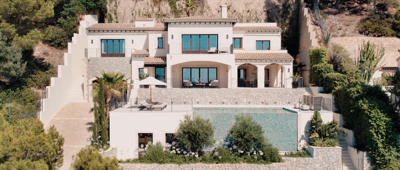 Vue extérieure d'une villa blanche à plusieurs niveaux avec une piscine à débordement et des murs en pierre.