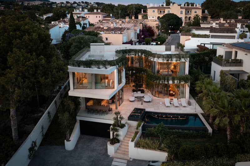 Vue aérienne d'une villa contemporaine blanche avec terrasses à niveaux, verdure intégrée et piscine au crépuscule.