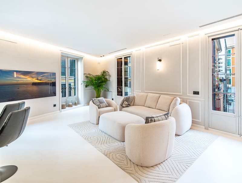 Salon moderne avec sièges en bouclé crème, moulures murales et portes-fenêtres ouvrant sur des balcons.