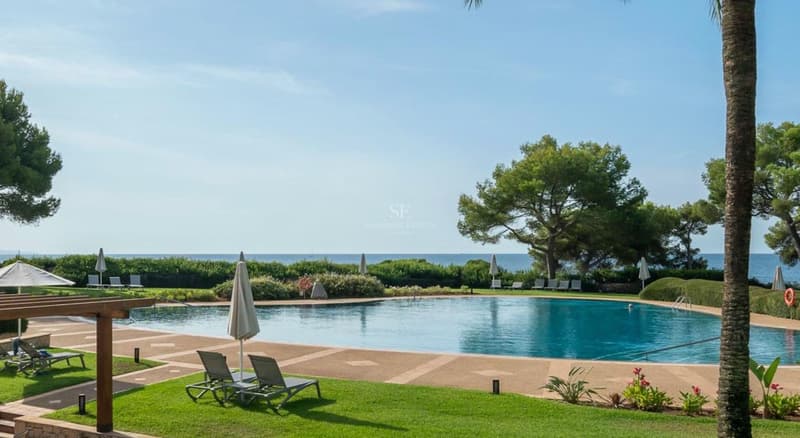 Großer blauer Swimmingpool umgeben von Steinterrasse, Rasen, Liegestühlen und Pinien mit Blick auf das Meer.