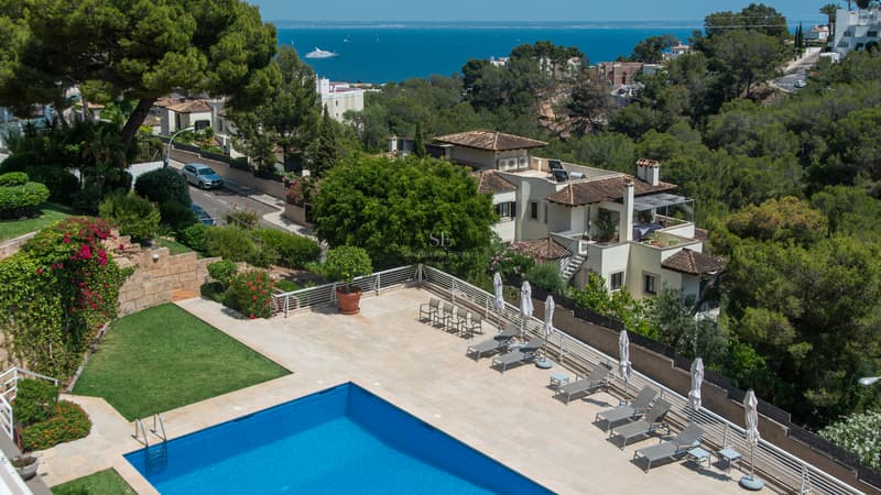 Vue aérienne d'une piscine bleue et terrasse avec chaises longues surplombant la Méditerranée et les villas.