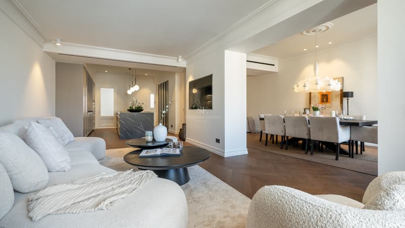 Salon contemporain avec parquet en chevrons, canapés bouclés blancs et îlot de cuisine en marbre au second plan.