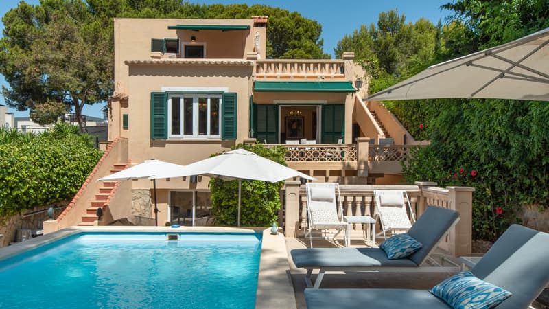 Vue extérieure d'une villa avec piscine turquoise, chaises longues et façade ocre aux volets verts.