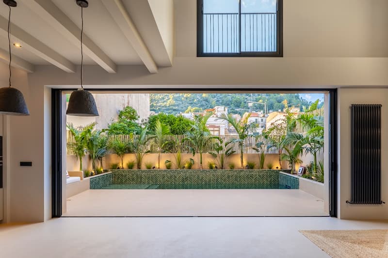 Salon Moderne avec Piscine Privée et Terrasse Tropicale Vue intérieure par une grande baie vitrée vers une piscine privée entourée de plantes tropicales et carrelage vert.