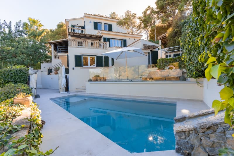Piscine privée devant une villa blanche de style méditerranéen avec volets verts et environnement boisé.