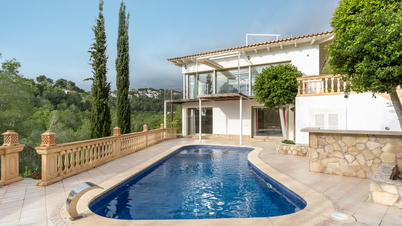 Villa méditerranéenne de luxe avec piscine privée Une piscine de forme libre sur une terrasse en pierre à côté d'une villa blanche de deux étages avec vue sur la forêt.