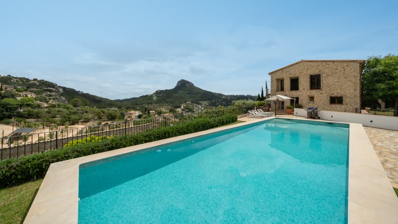 Piscine de Luxe avec Vue Panoramique sur la Montagne Grande piscine rectangulaire surplombant une vallée verdoyante et des montagnes avec une villa en pierre.