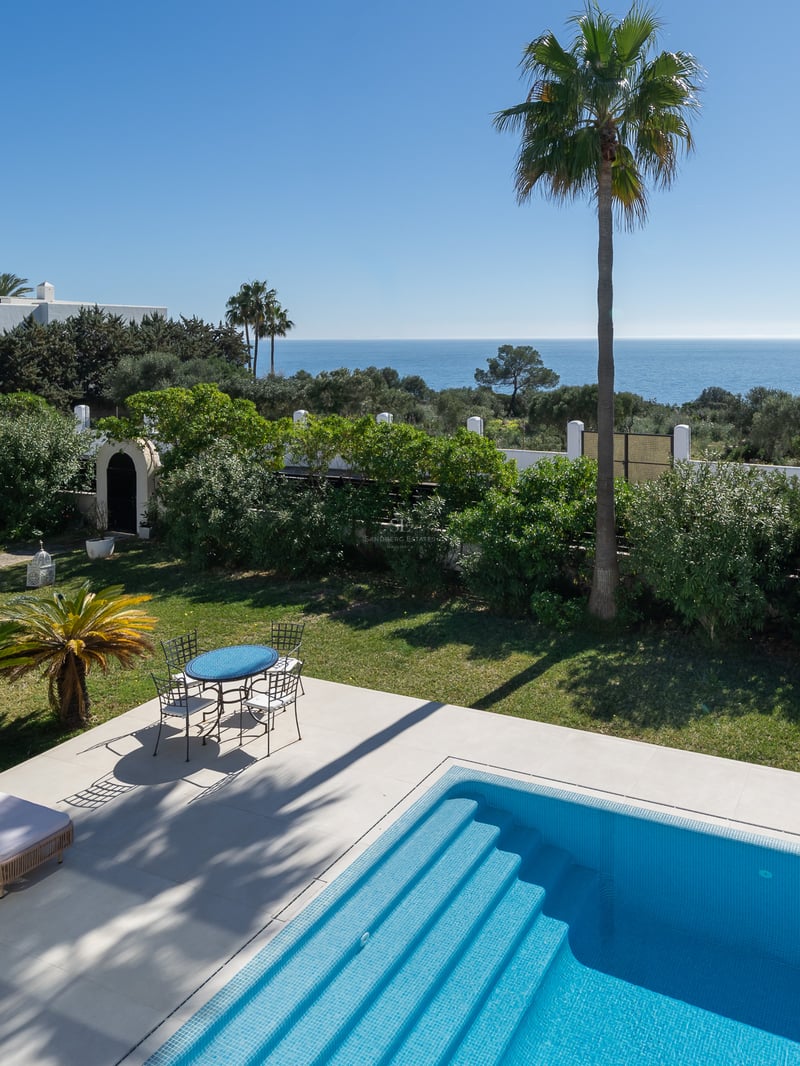 Piscine bleue étincelante et mobilier de jardin surplombant un jardin luxuriant et la mer Méditerranée.