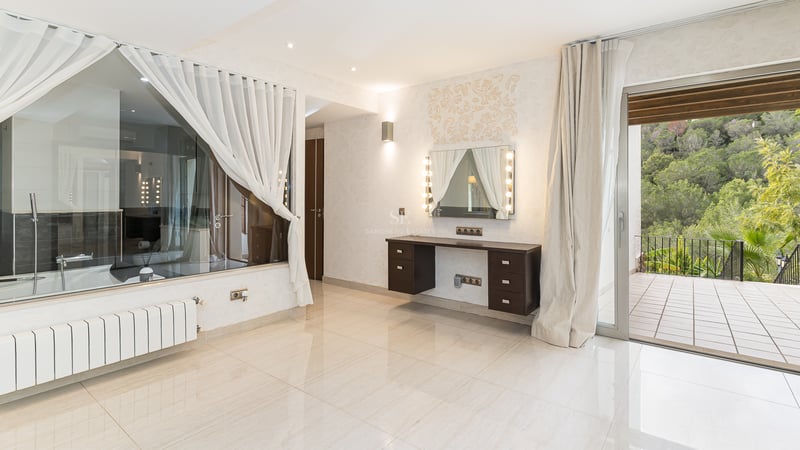 Espace dressing lumineux avec coiffeuse miroir Hollywood, paroi vitrée vers la salle de bain et terrasse vue forêt.