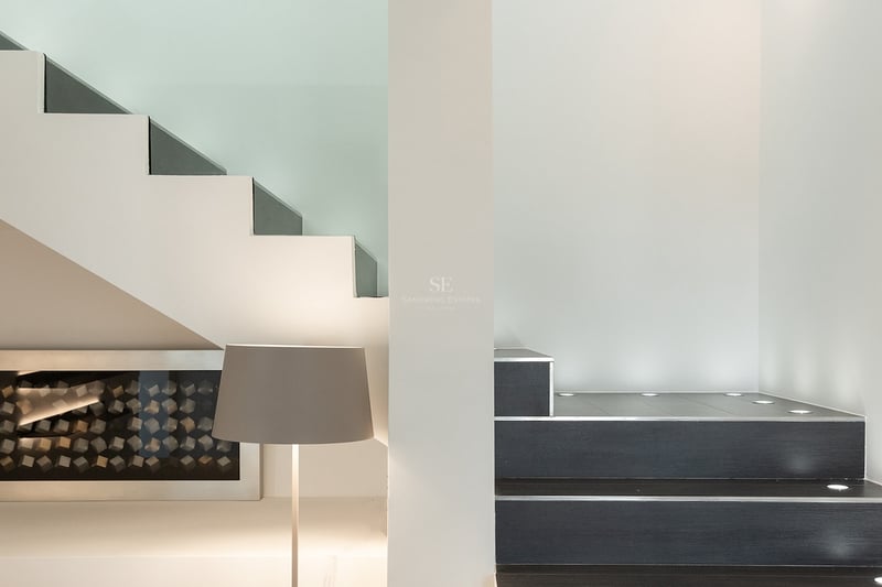 Gros plan d'un escalier minimaliste avec des marches sombres, des murs blancs et des spots LED encastrés au sol.