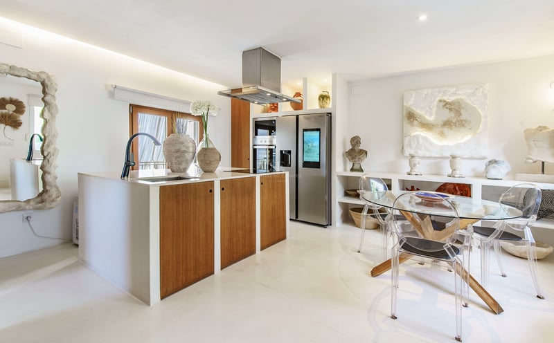 Cuisine moderne avec îlot en bois, appareils en acier inoxydable et table à manger en verre avec chaises transparentes.