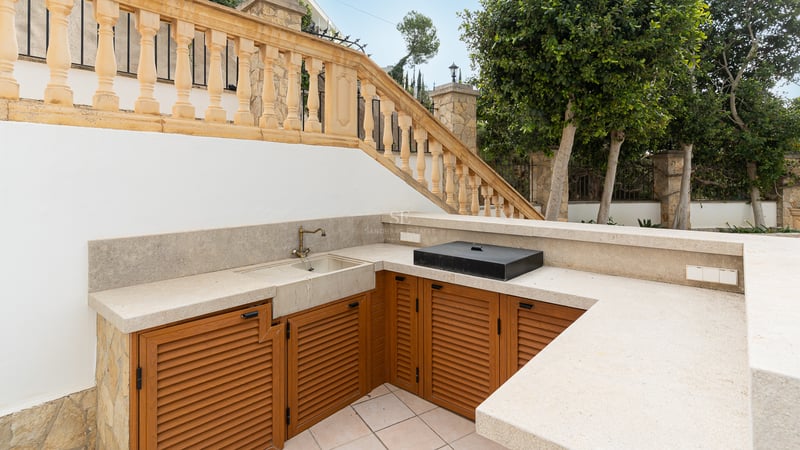 Cuisine extérieure avec plans de travail en pierre, meubles en bois et évier en laiton près d'une balustrade classique.