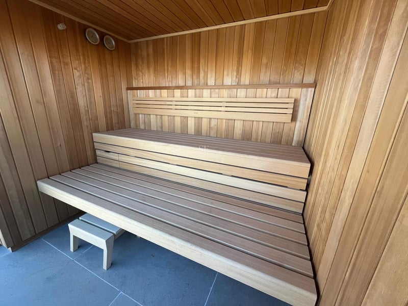 Intérieur d'un sauna moderne en bois avec banquettes à deux niveaux et carrelage de sol gris.