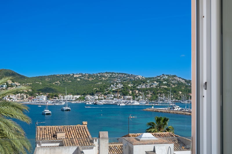 Vue d'un port méditerranéen rempli de yachts, d'eaux turquoise et de villas à flanc de colline sous un ciel bleu.