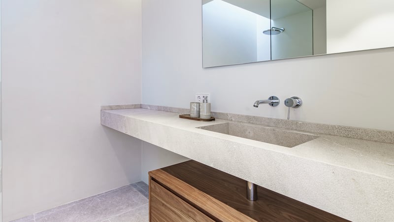 Salle de bain moderne avec vasque suspendue en pierre naturelle, robinetterie chromée et meuble en bois.